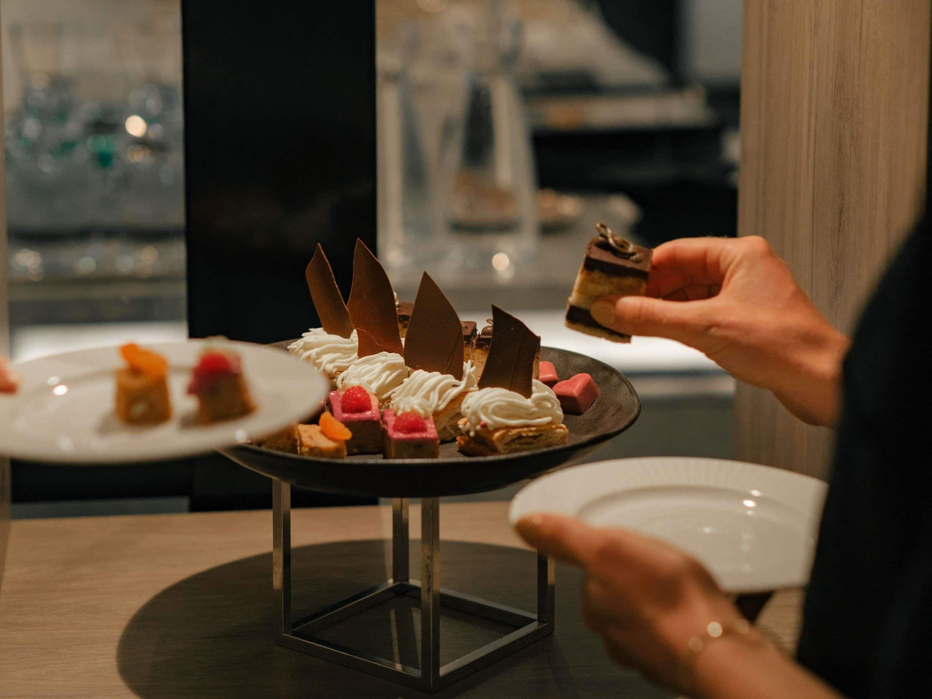 A dessert display with various pastries and a person holding a piece.
