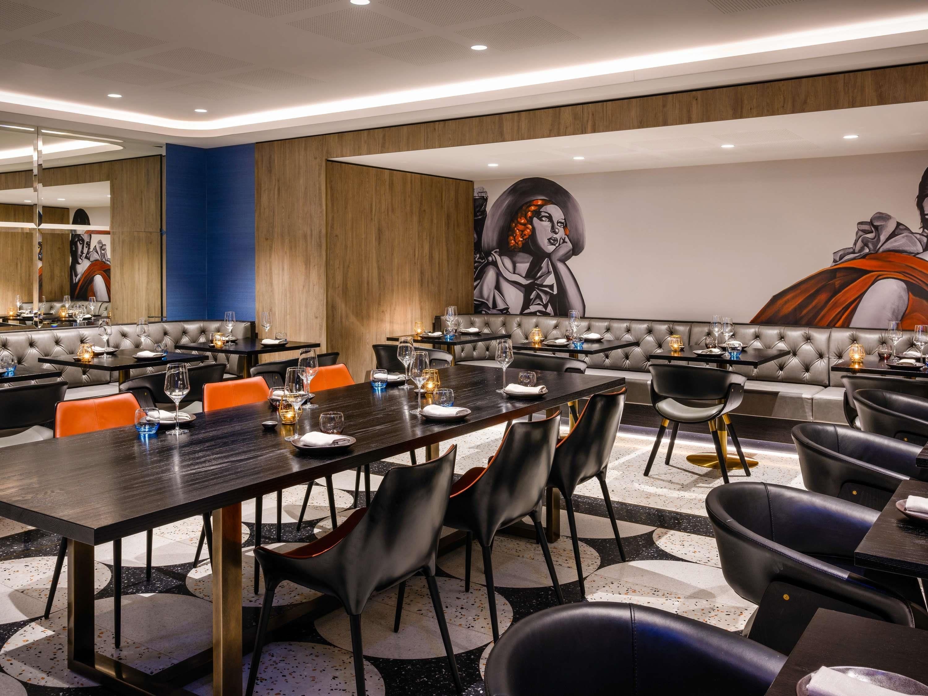 A modern restaurant with leather booths, black and orange chairs, and a large mural on the wall.