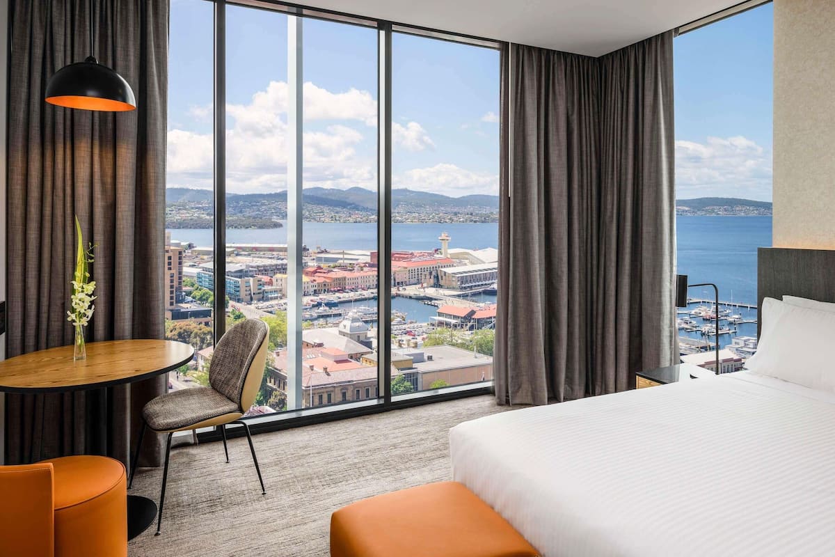 Een hotelkamer met een groot raam, een bed, een ronde tafel en een stoel.
