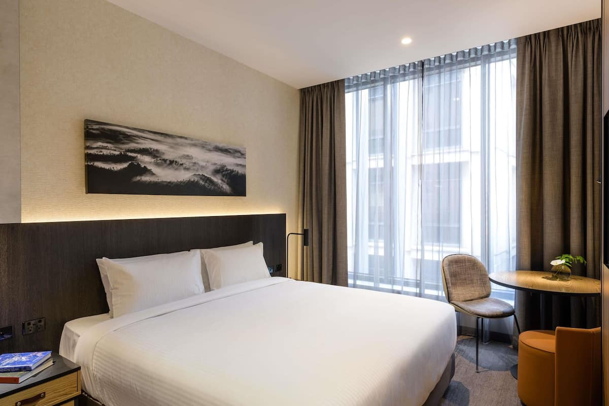 Een hotelkamer met een groot bed, een stoel, een klein tafeltje en een schilderij aan de muur.