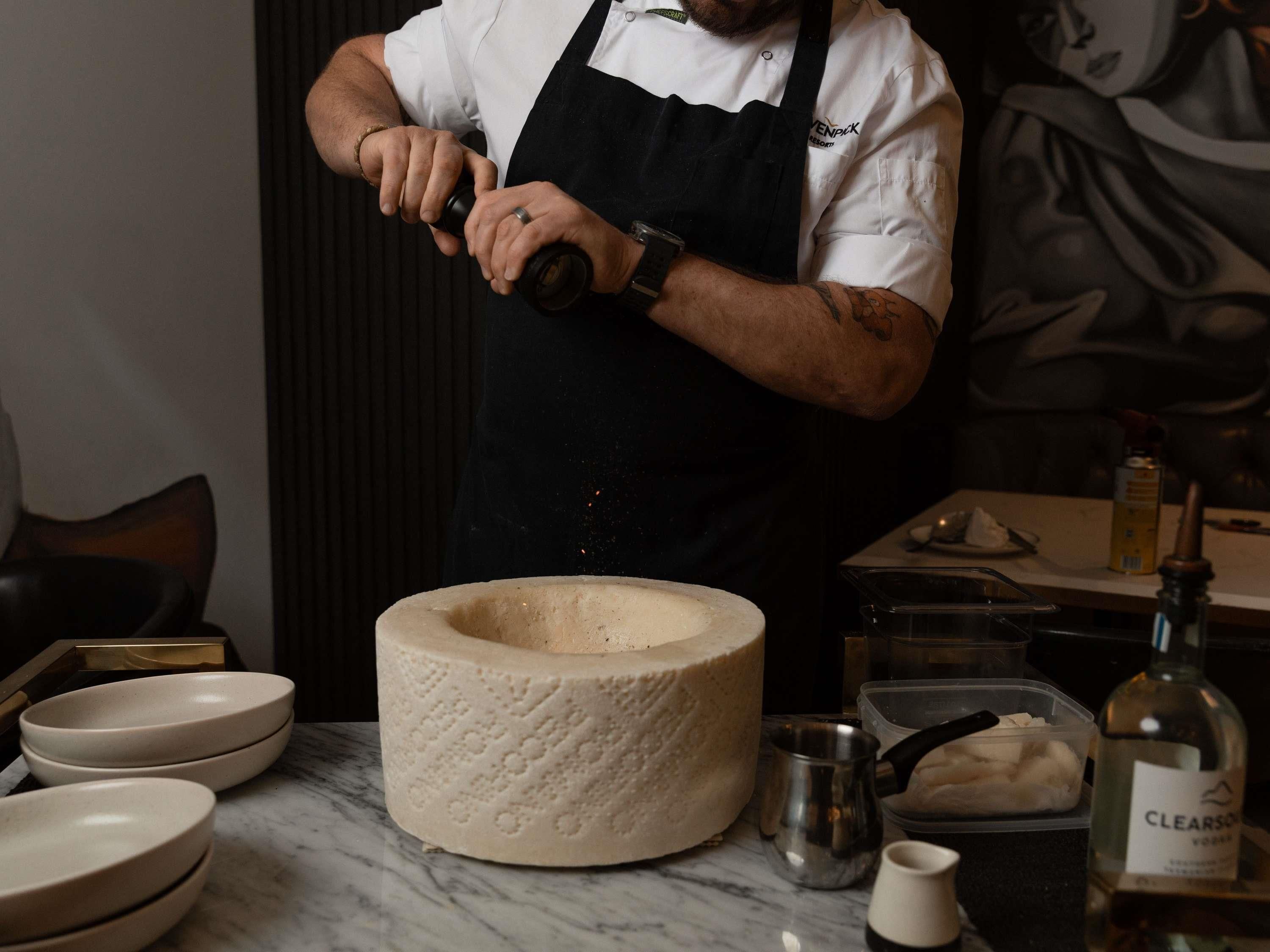 A person in a chef's uniform preparing food, with a large stone bowl, a bottle of Clearsound vodka, and various kitchen utensils on the counter.