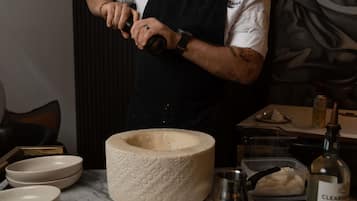 A person in a chef's uniform preparing food, with a large stone bowl, a bottle of Clearsound vodka, and various kitchen utensils on the counter.