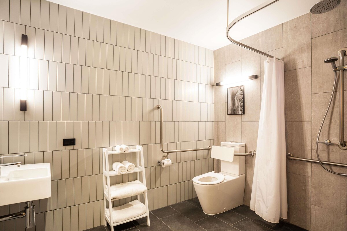 Een moderne badkamer met douche, toilet en wastafel, met betegelde wand en een witte handdoekhouder.
