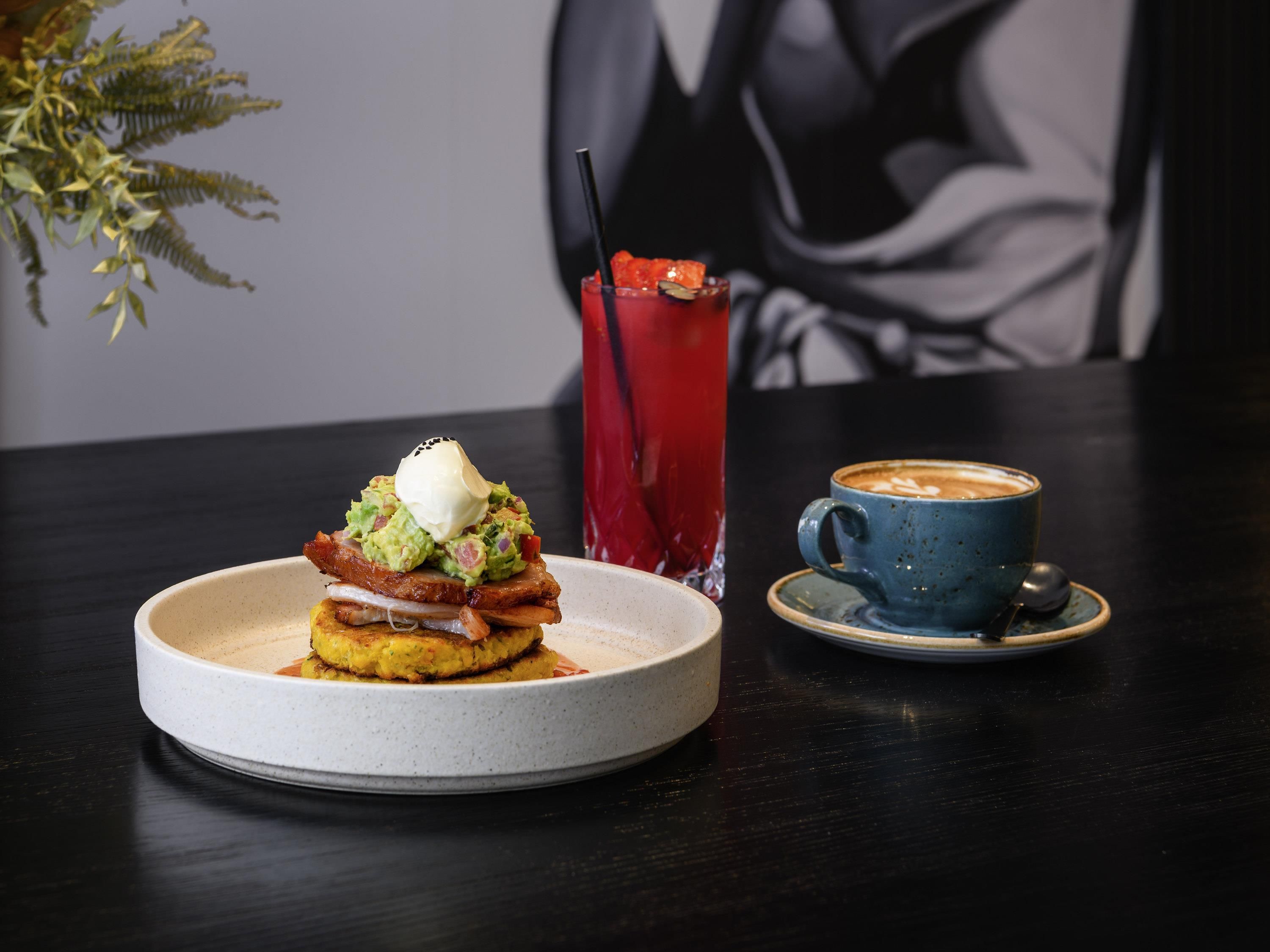 A plate of food with a poached egg and avocado, a glass of red drink, and a cup of coffee on a table.