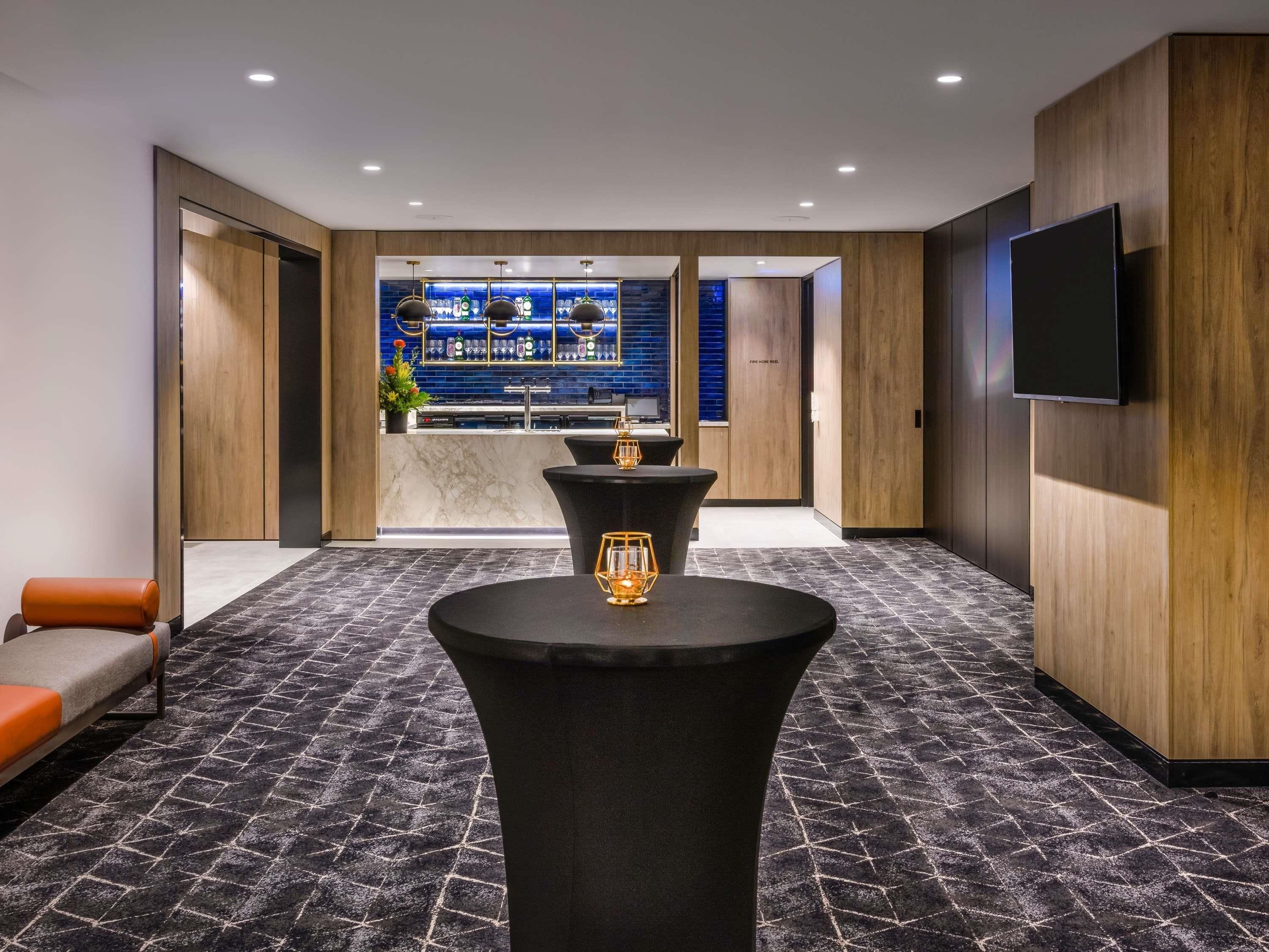 A modern hotel lobby with a bar area, seating, and a TV mounted on the wall.