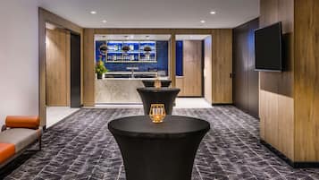 A modern hotel lobby with a bar area, seating, and a TV mounted on the wall.