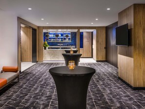 Un moderno vestíbulo de hotel con zona de bar, asientos y un televisor montado en la pared.