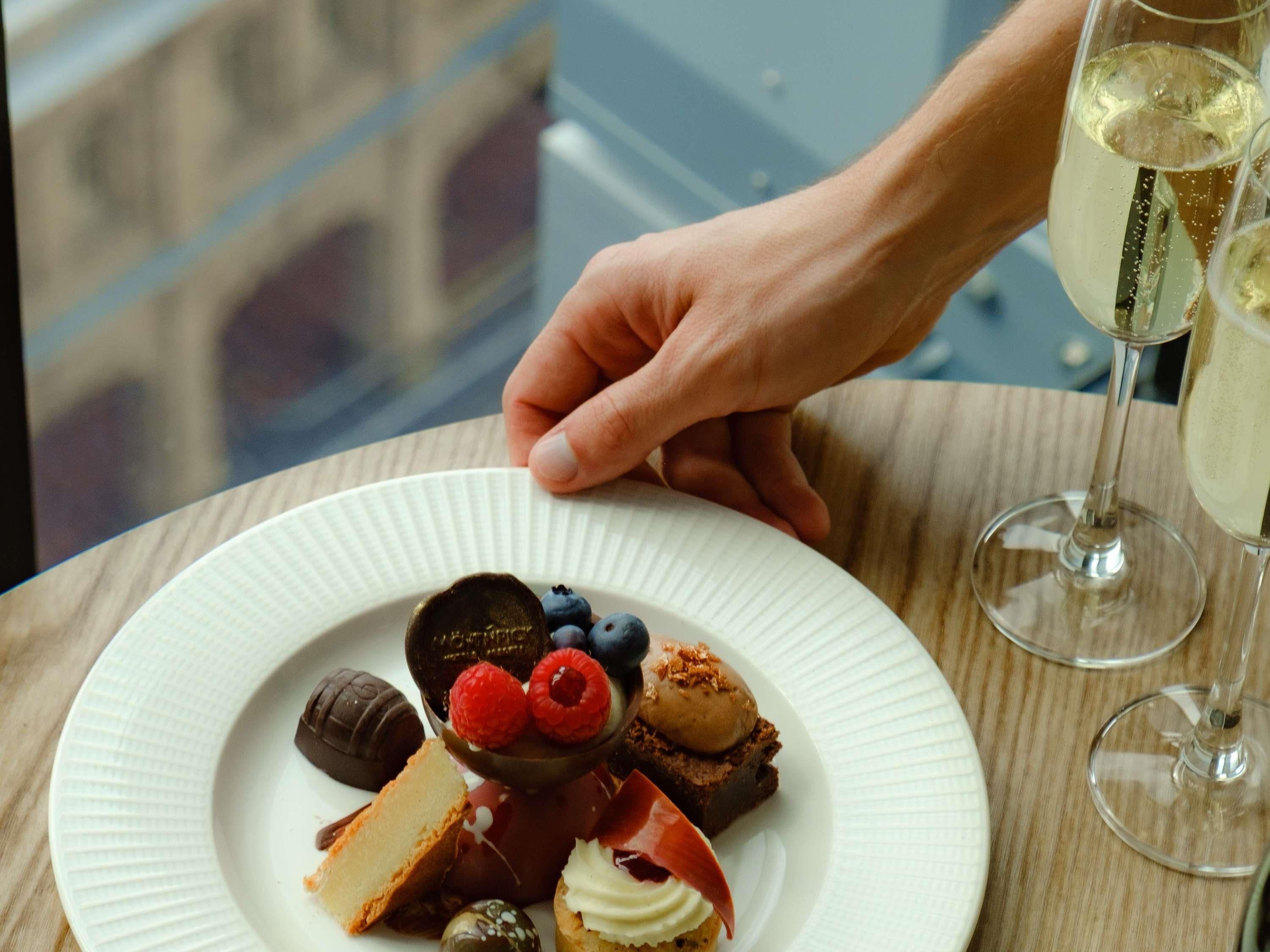 Un plato de postres variados y dos copas de vino blanco sobre una mesa.