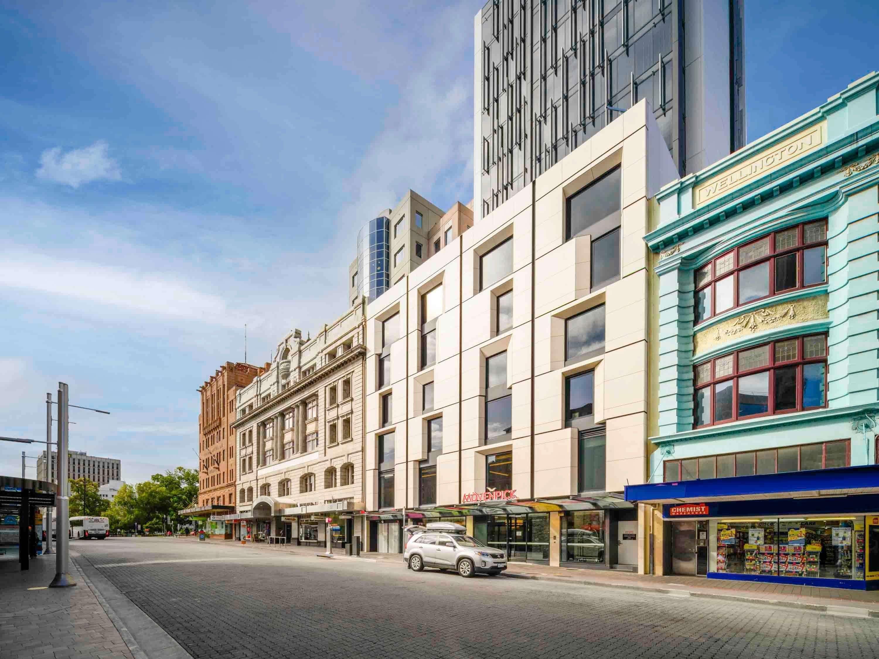 A street view with a modern building, a bus stop, and a chemist shop.