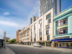 Vista de la calle con un edificio moderno, una parada de autobús y una farmacia.