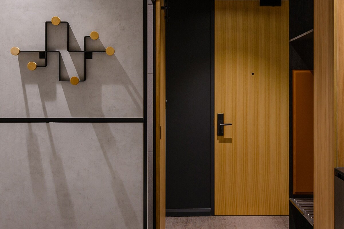 Una habitación moderna con una obra de arte geométrica en la pared, una puerta de madera y suelo cubierto de alfombra.