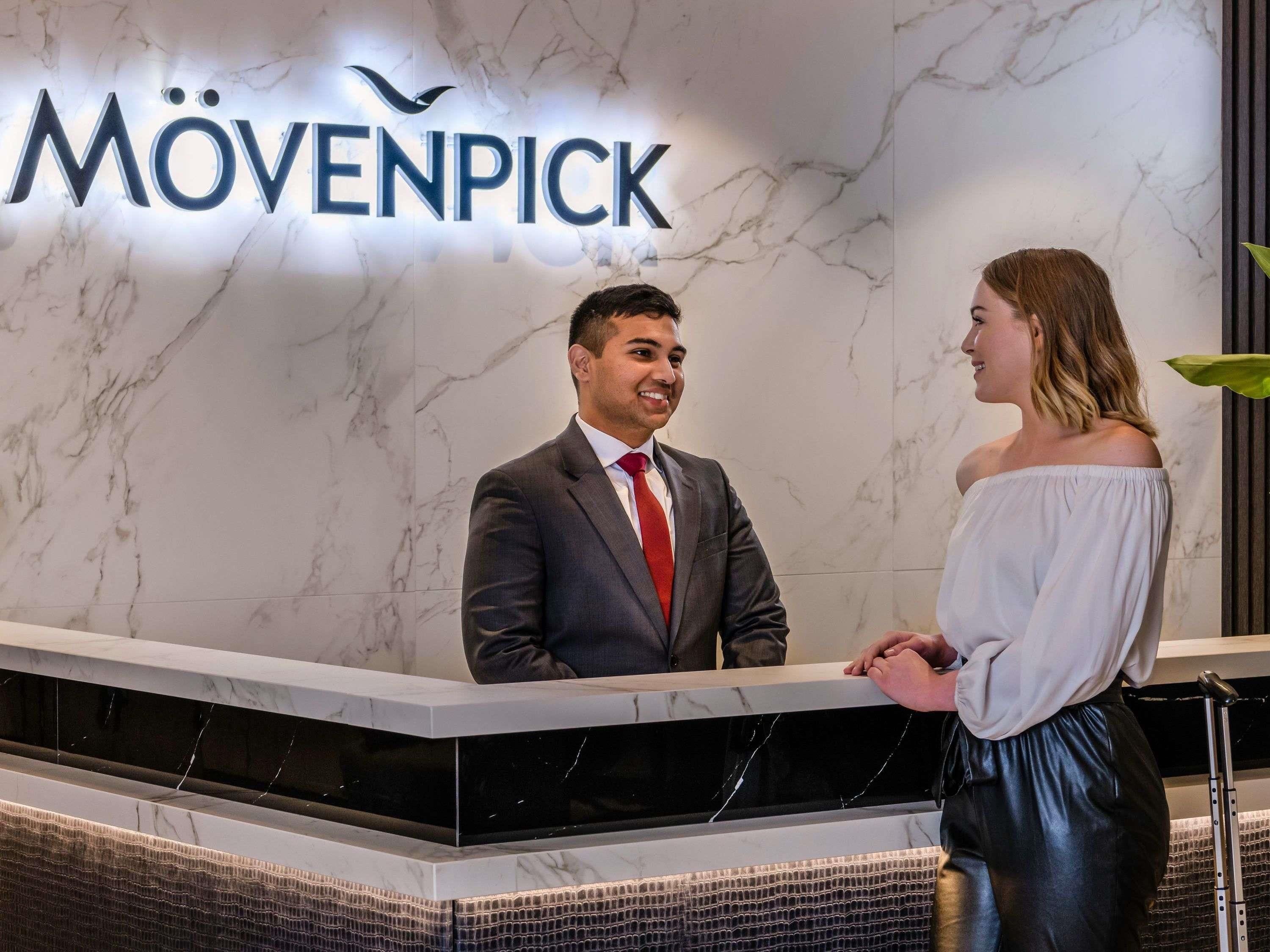 A reception desk with a marble wall and the sign 'MÖVENPICK' above it.