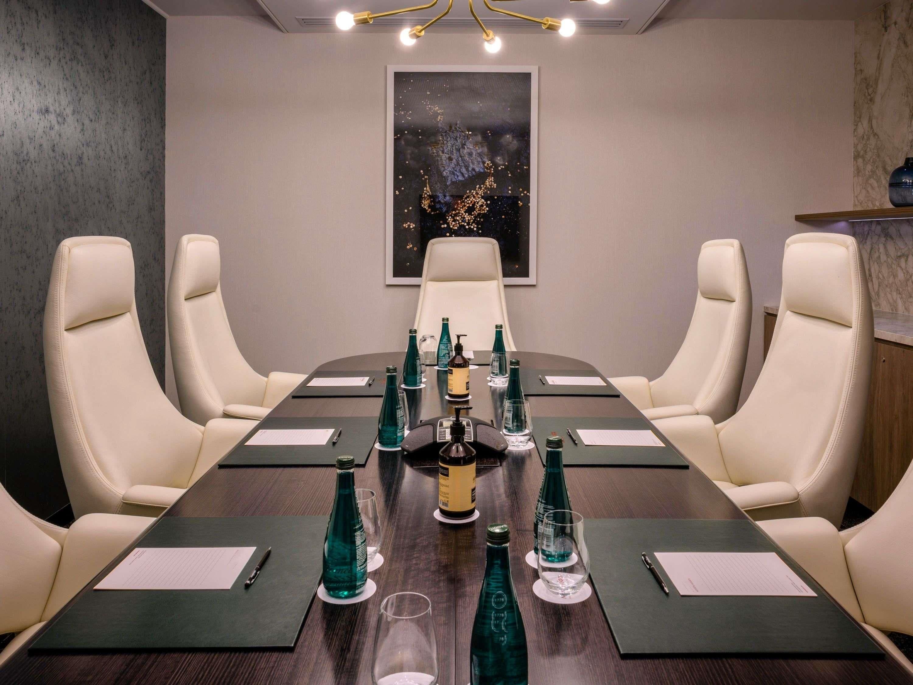 A conference room with a long table, four chairs, and a painting on the wall.