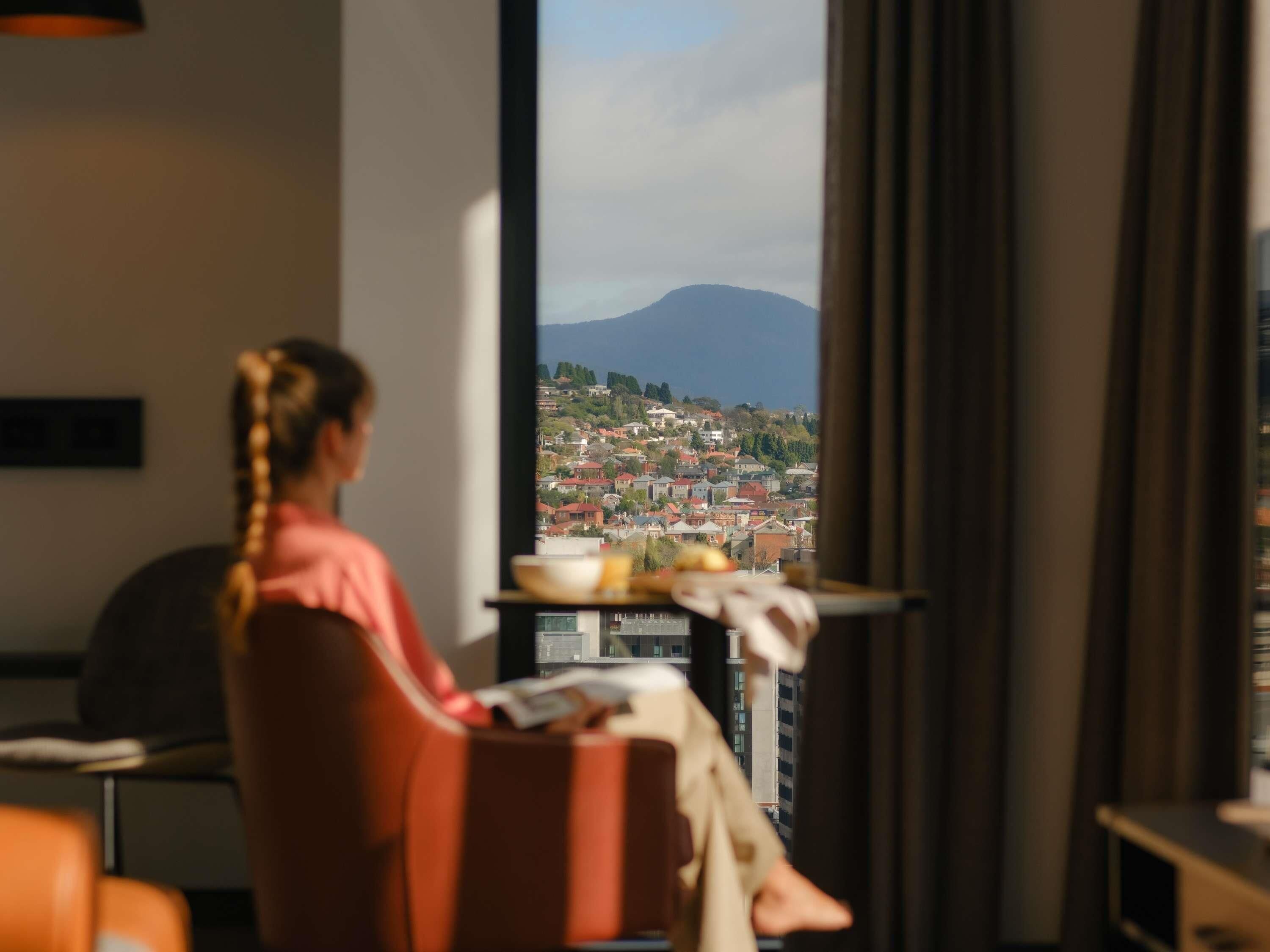 A person sitting by a window with a view of a cityscape and a mountain.