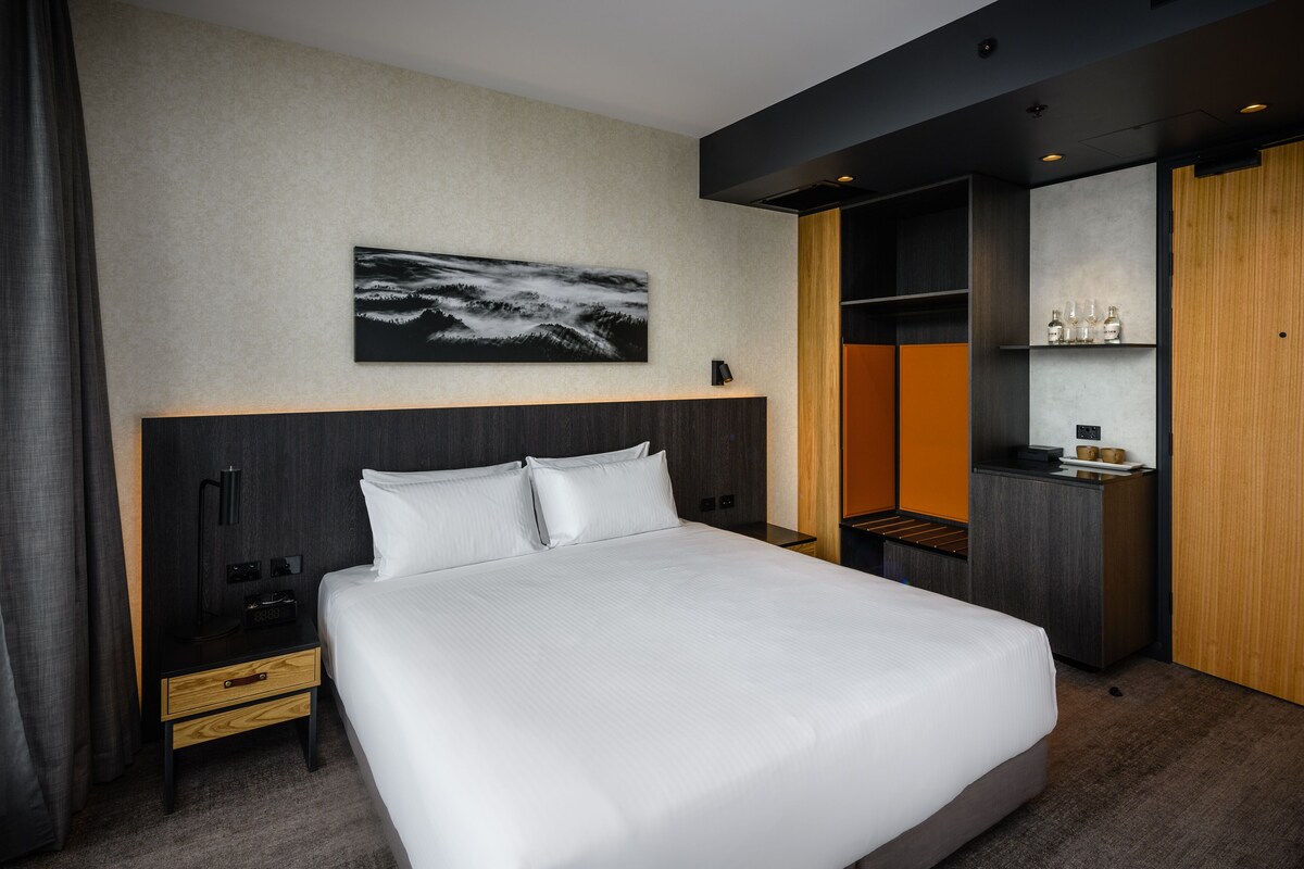 Una habitación de hotel moderna con una cama grande, una mesita de noche, un escritorio y un armario.