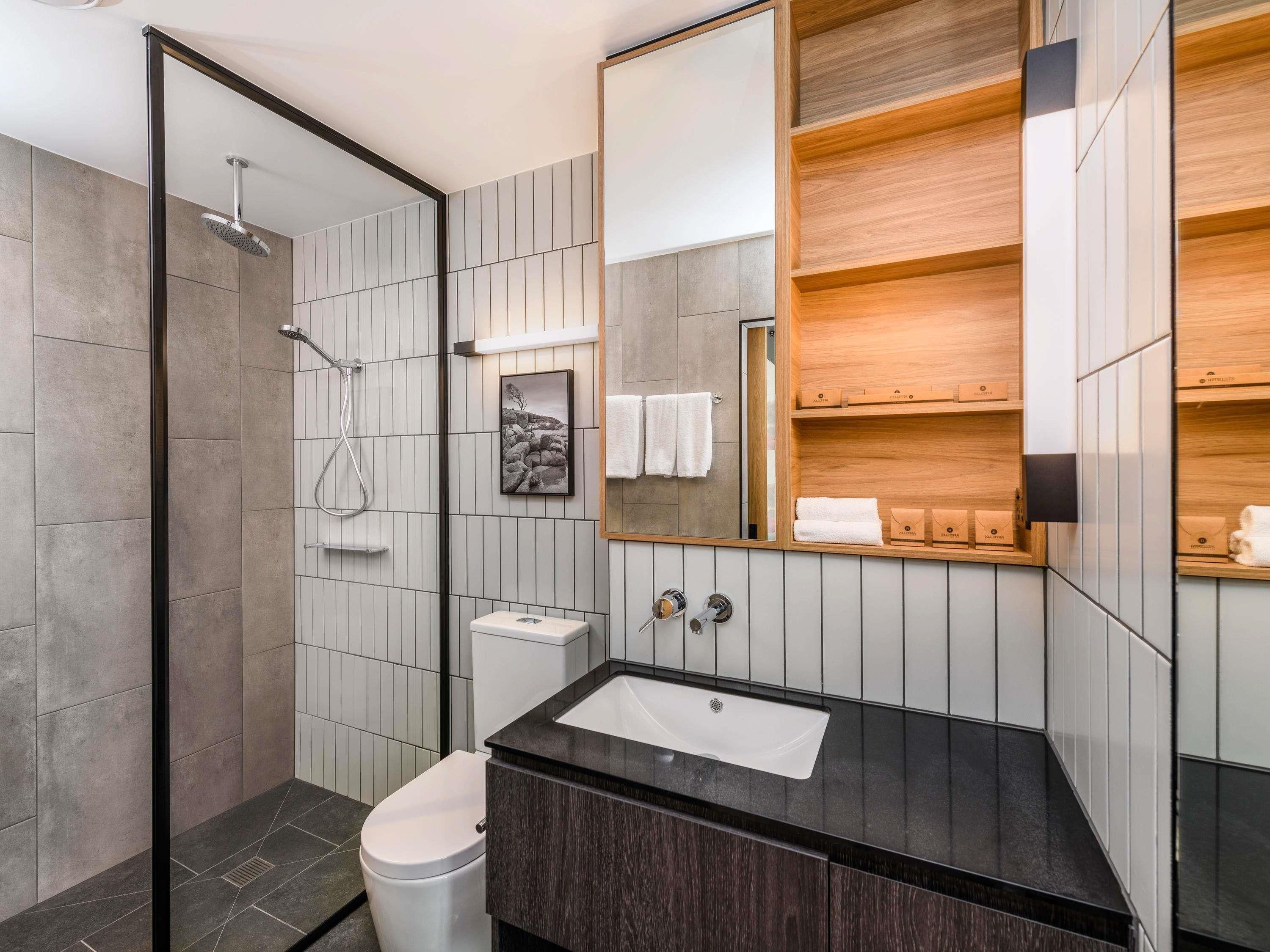 A modern bathroom with a shower, toilet, sink, and wooden vanity.