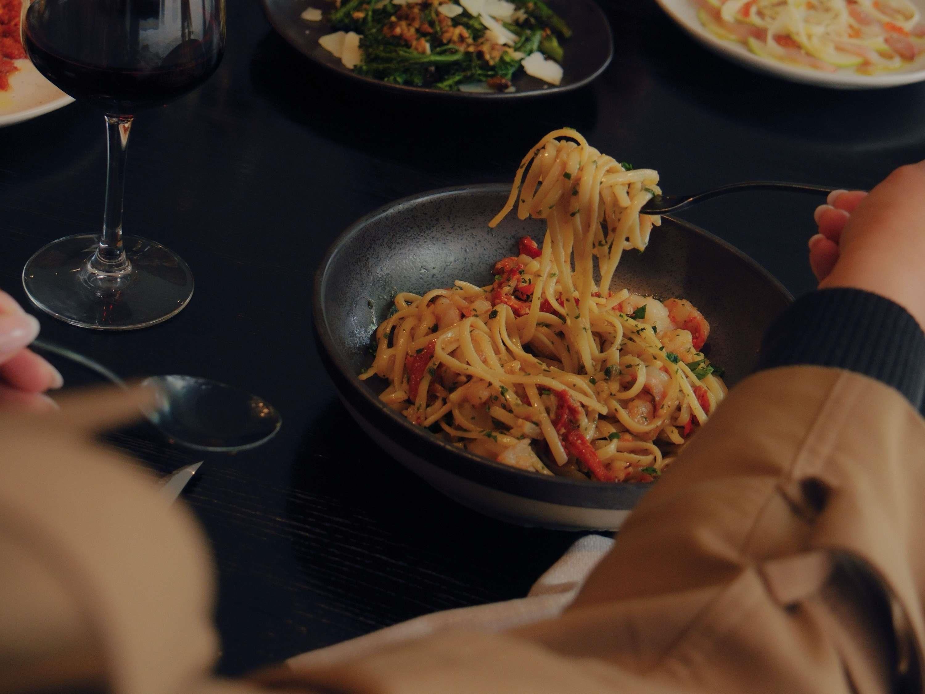 A dining table with a plate of spaghetti, a wine glass, and another plate with a salad.