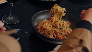 A dining table with a plate of spaghetti, a wine glass, and another plate with a salad.
