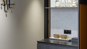 Et moderne hotelværelse med et mørkegråt konsolbord, to beige kopper og en flaske Cape Grim vin på en hylde.