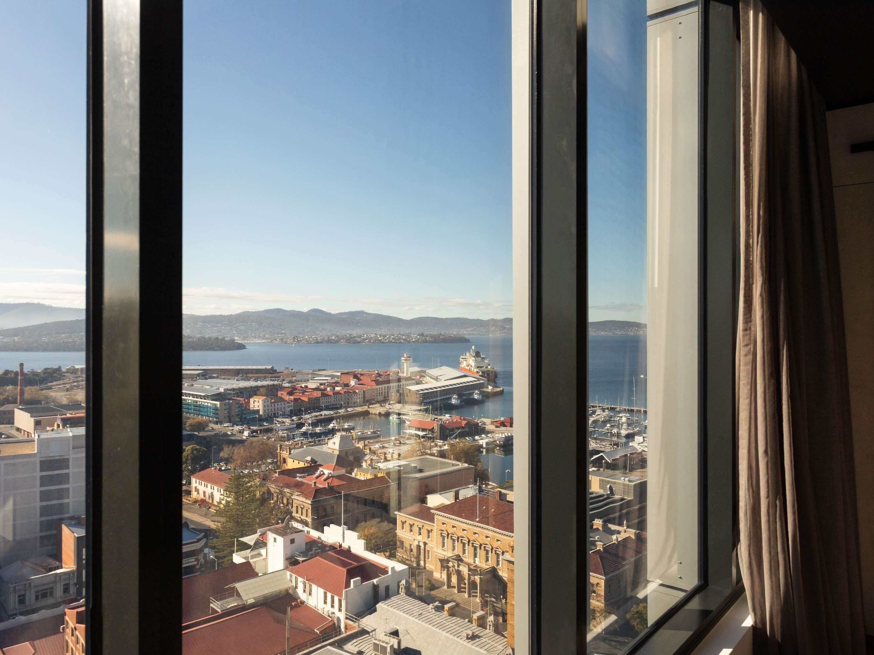 Une vue à travers une fenêtre sur un paysage urbain, avec des bâtiments, un port et un phare.