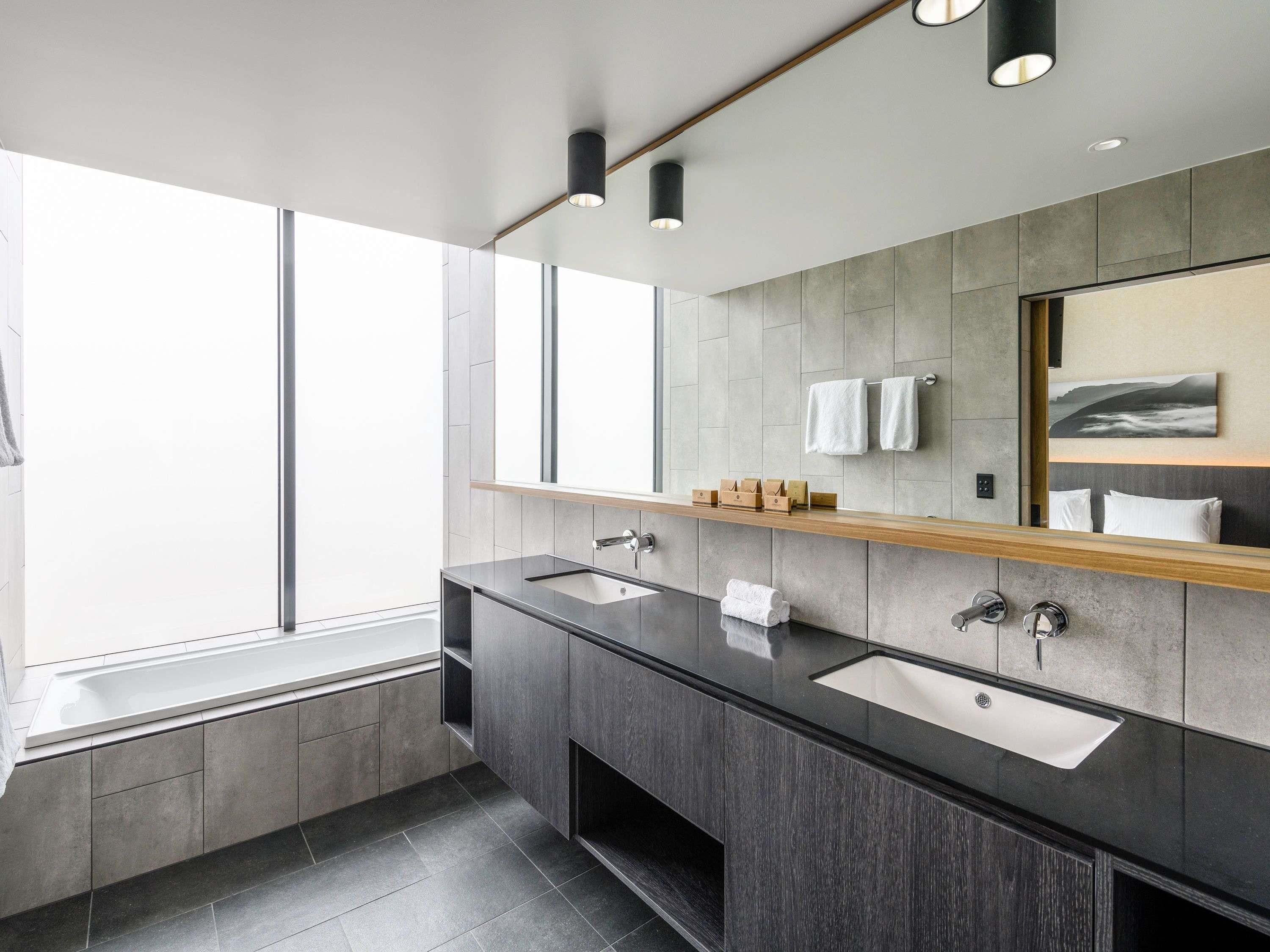 A modern bathroom with two sinks, a large mirror, and a window.