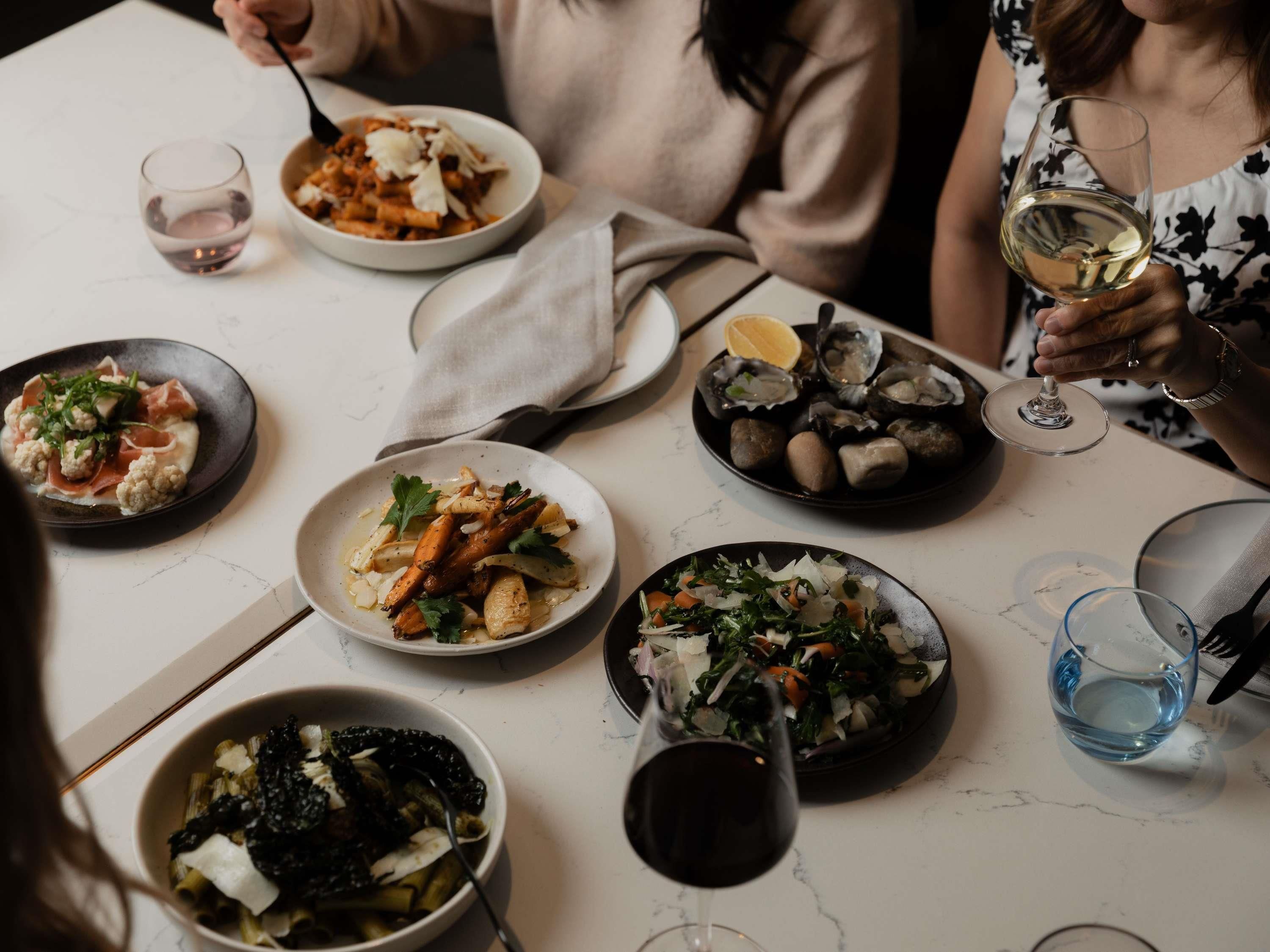 A dining table with various dishes and glasses of wine.