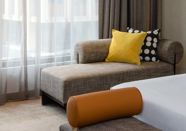 Een moderne hotelkamer met een slaapbank, een geel kussen en een bruin voetenbankje.