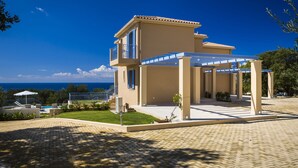 A two-story house with a balcony, a covered patio, and a view of the sea.