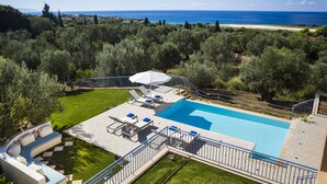 A pool area with lounge chairs and a view of the sea.