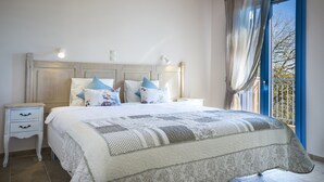 A bedroom with a large bed, two bedside tables, a nightstand, a window with curtains, and a view of the outdoors.