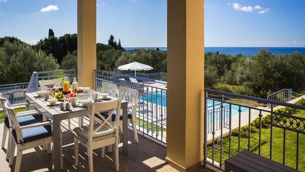 A terrace with a table set for breakfast, overlooking a swimming pool and the sea.