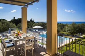 A terrace with a table set for breakfast, overlooking a swimming pool and the sea. - No 2 Forget Me Not Villa with private pool in stunning location (Svoronata)