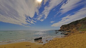 A beach with clear skies, a sandy shore, and rocky outcrops.