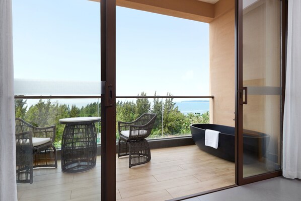 A balcony with wicker furniture, a round table, and a black bathtub with a towel.
