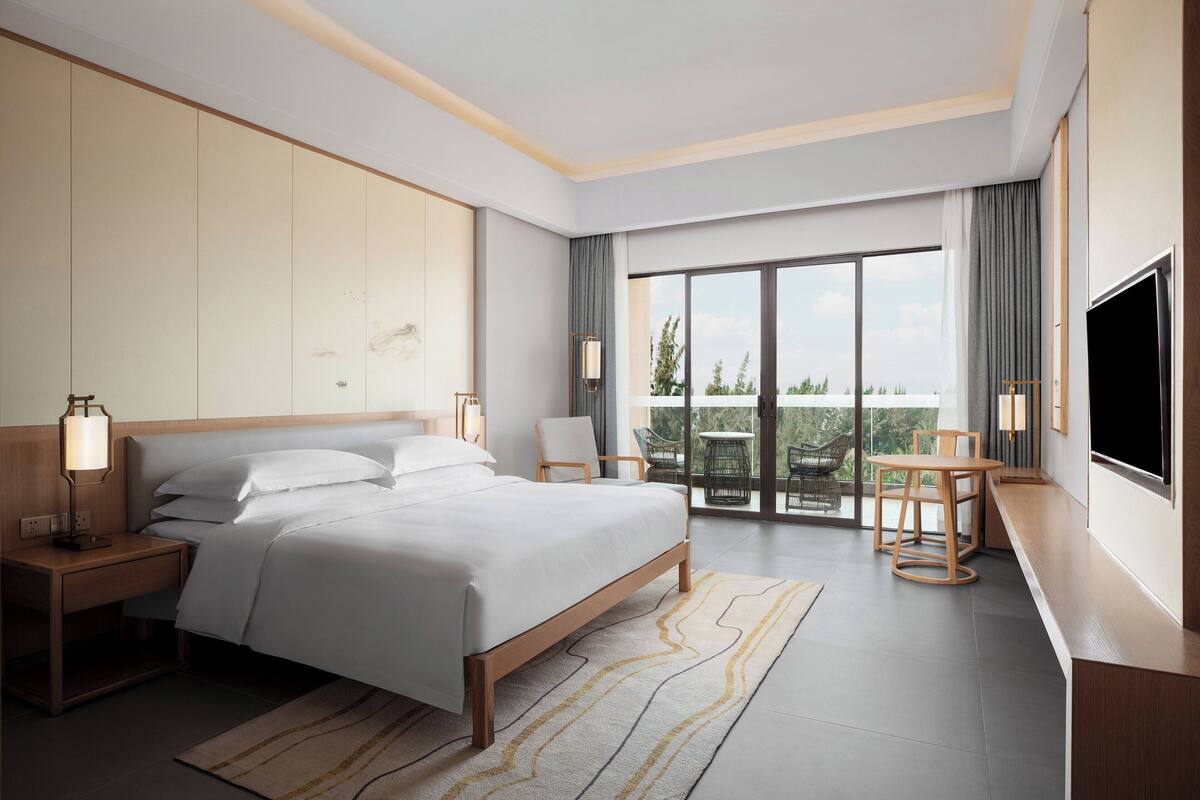 Ein modernes Hotelzimmer mit einem großen Bett, Nachttischen, einem Schreibtisch und einem Balkon mit Sitzgelegenheit.