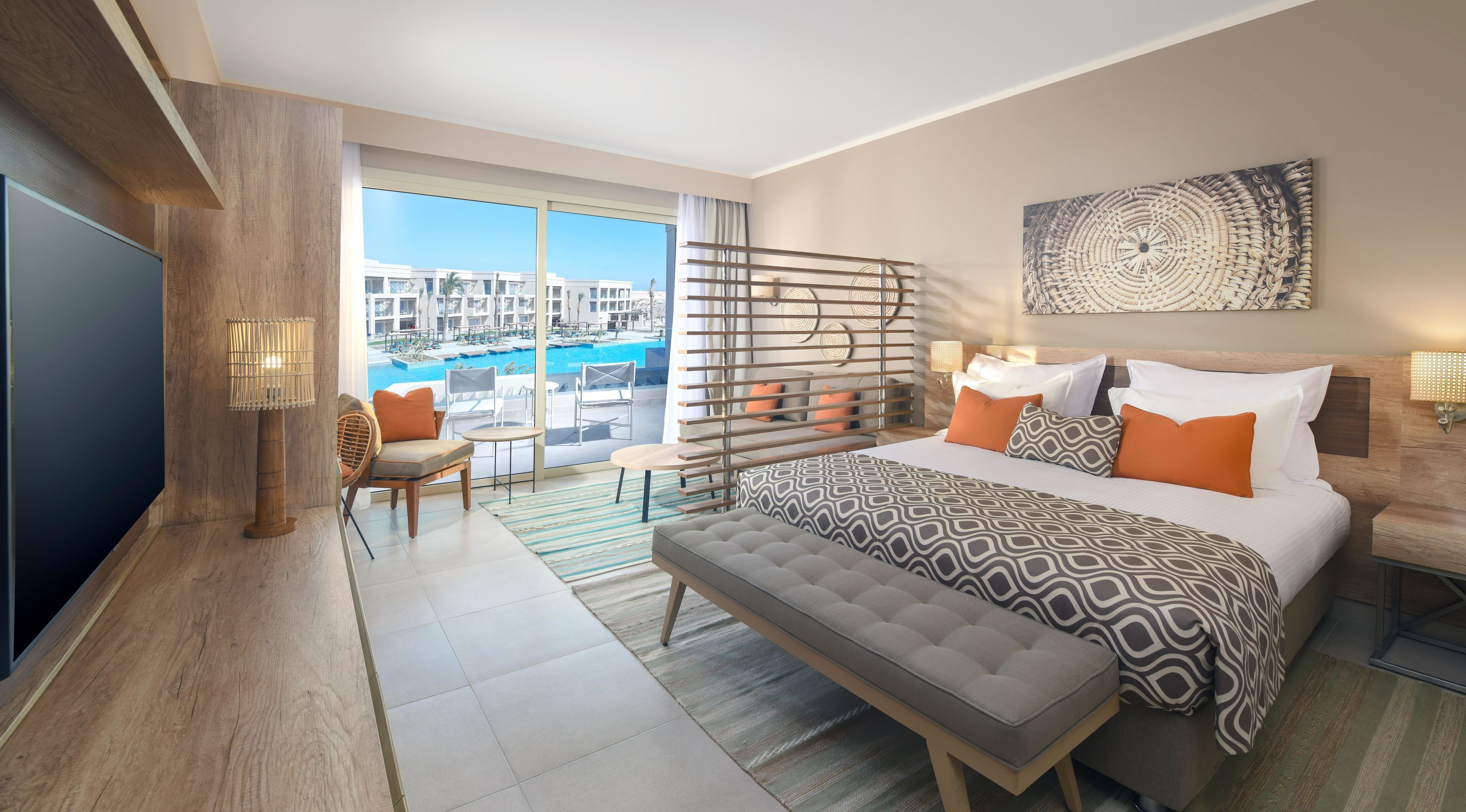 A hotel room with a large bed, a seating area with a view of a pool, and a balcony with a view of buildings.