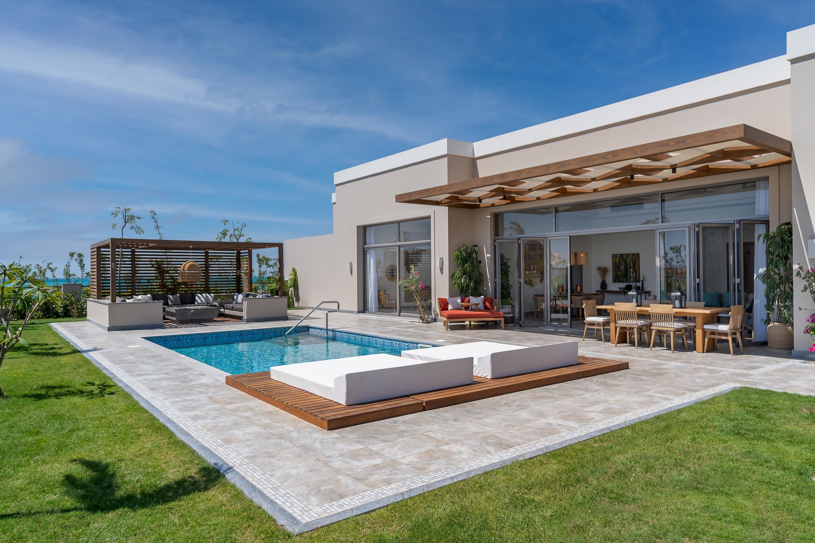 Una casa moderna con piscina, mobiliario de exterior y un porche cubierto.