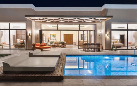 A modern house with a swimming pool, outdoor seating, and a well-lit interior.
