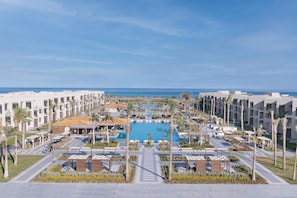 Resort com piscina central, vários edifícios e palmeiras.