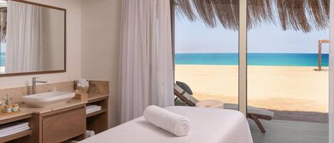 A hotel room with a large bed, a bathroom with a sink and mirror, and a view of the beach.
