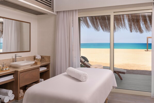 A hotel room with a large bed, a bathroom with a sink and mirror, and a view of the beach.