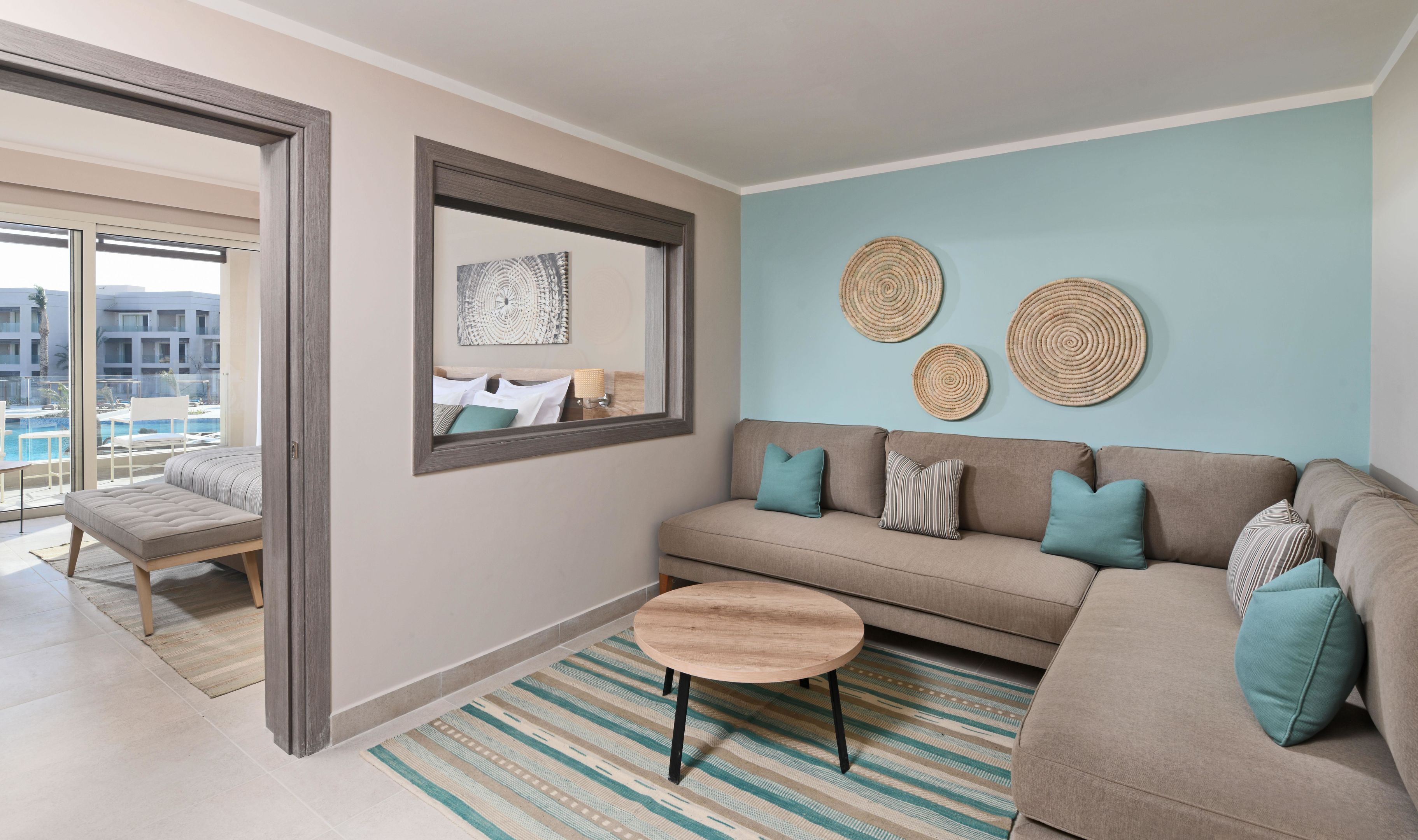 Een moderne woonkamer met een bank, een ronde salontafel en een groot raam met uitzicht op een zwembad.