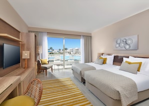 A hotel room with a large bed, a TV, a desk, and a view of a pool and buildings.