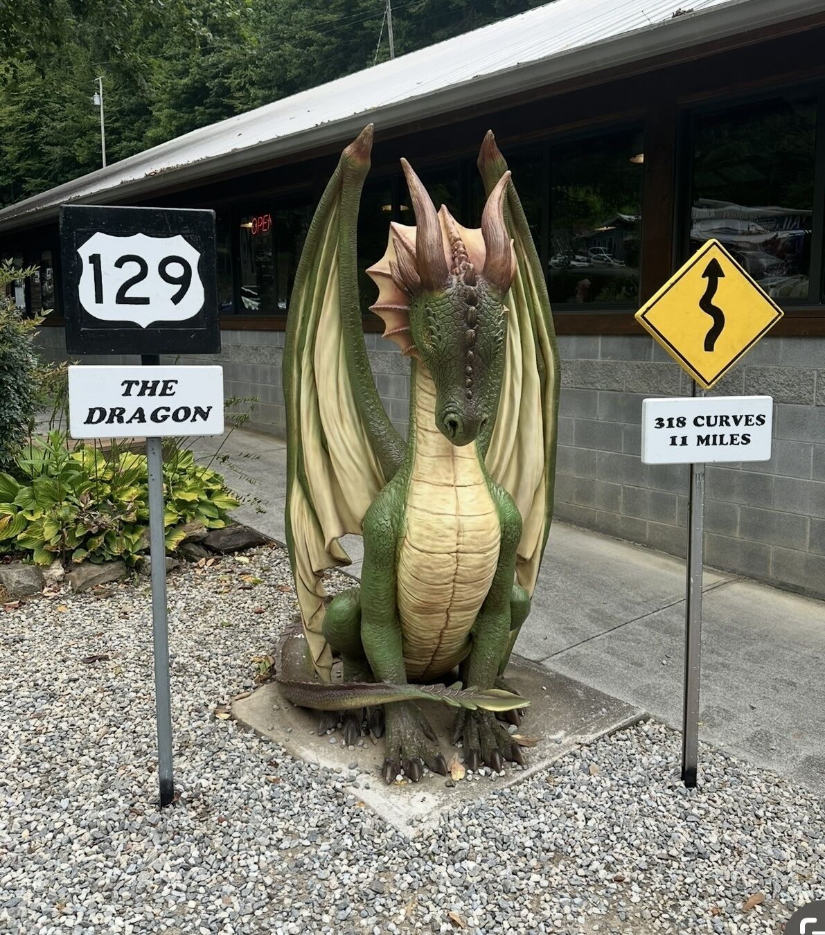 A dragon sculpture with road signs indicating '129 The Dragon' and '318 Curves 11 Miles'.