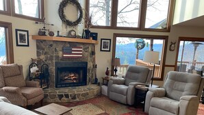 A cozy living room with a stone fireplace, comfortable seating, and a view of the outdoors. - Bear's Mountaintop Views 3 Bedroom Chalet by RedAwning (Robbinsville)
