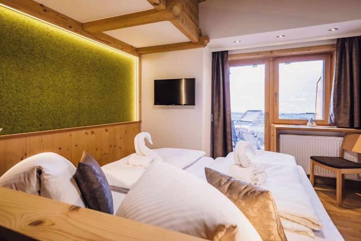 A hotel room with two beds, a television, a view of the outdoors, and a wooden ceiling.