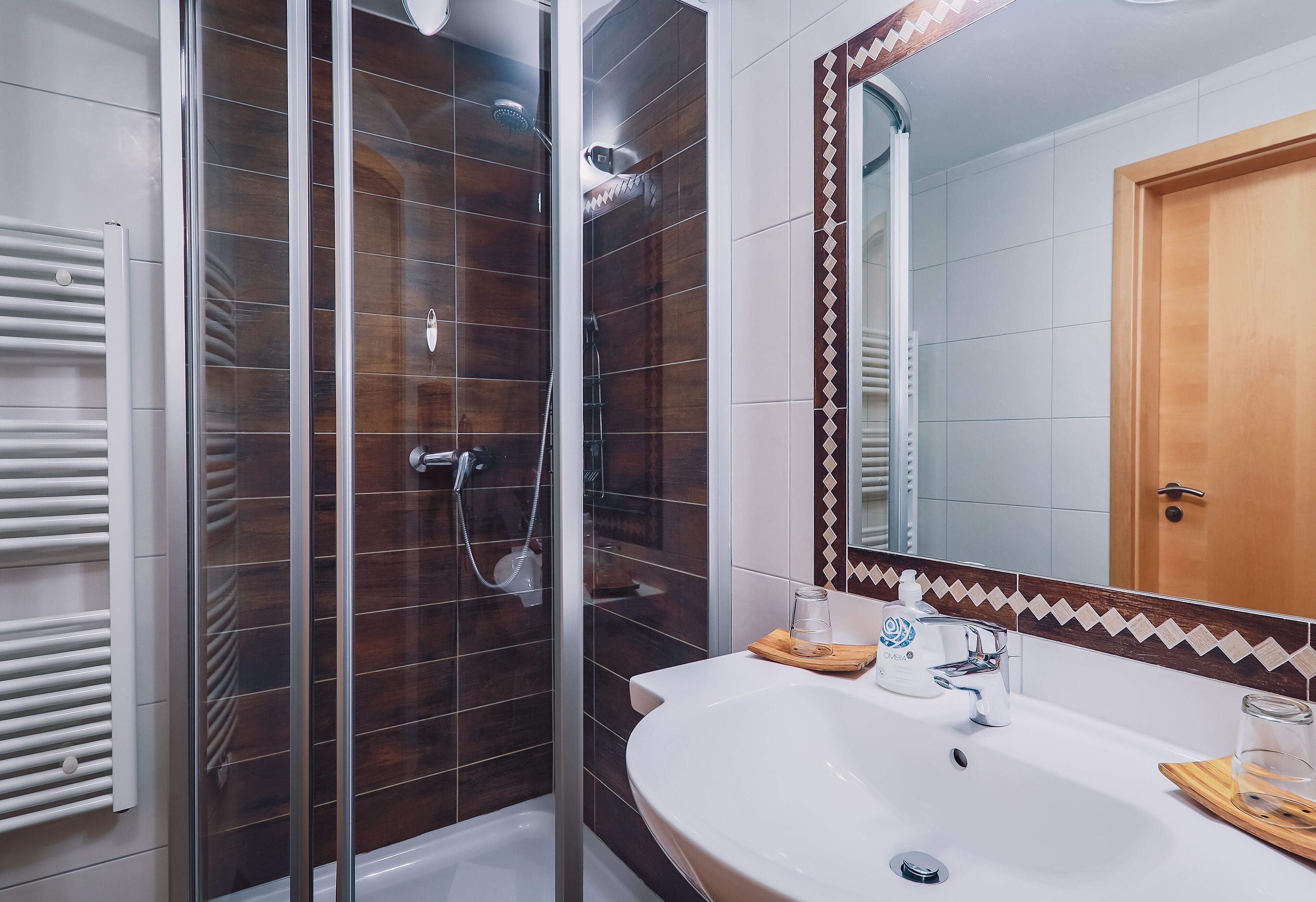 A modern bathroom with a glass-enclosed shower, a white sink, and a mirror with a decorative tile border.