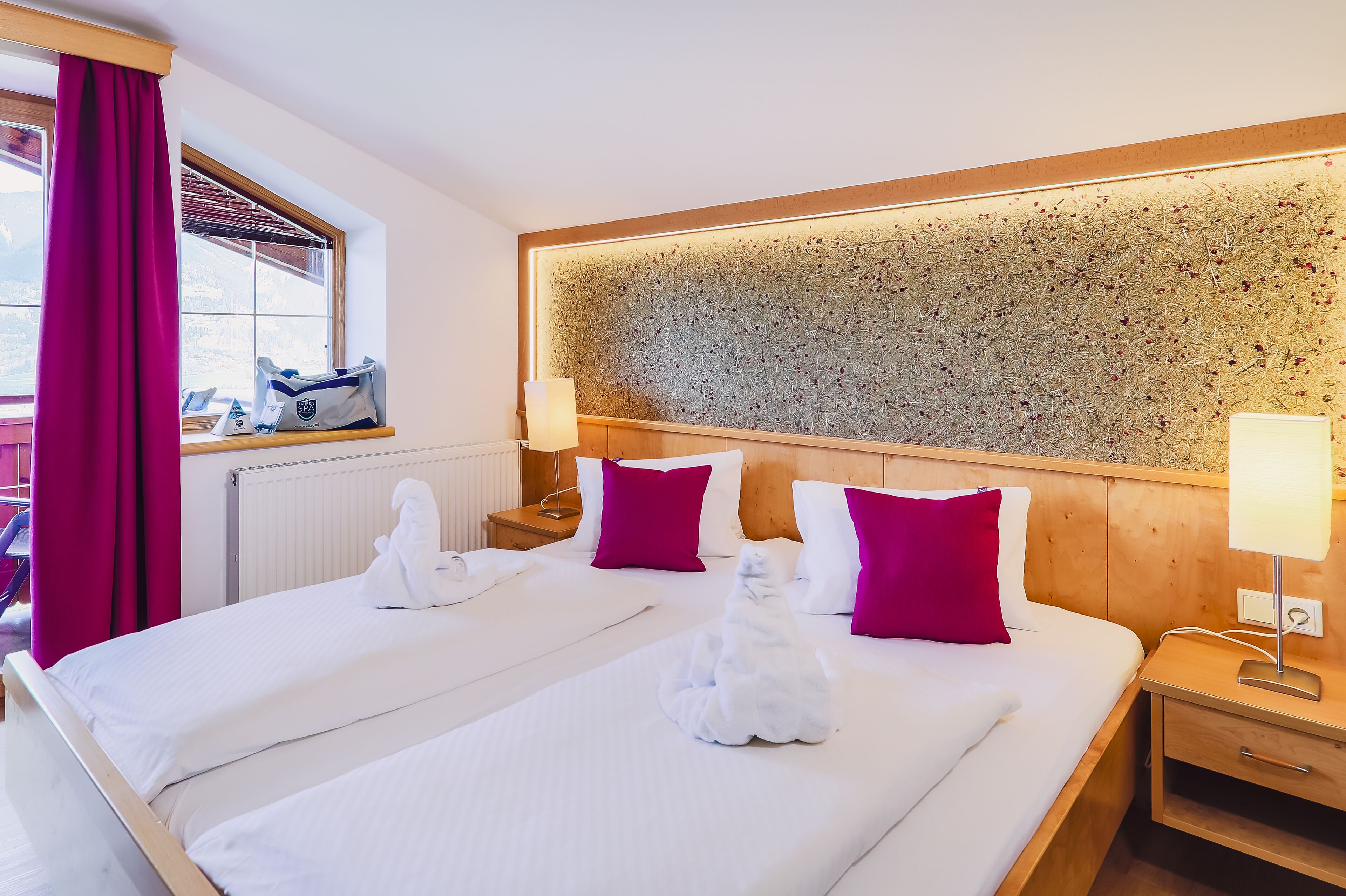 A hotel room with a large bed, two pillows, a nightstand, a lamp, and a window with a view.