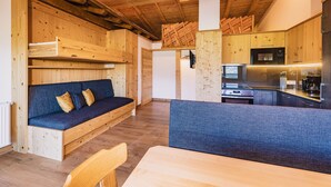 Un espace de vie compact doté d’un plafond en bois, d’un canapé, d’une table à manger et d’un coin cuisine.