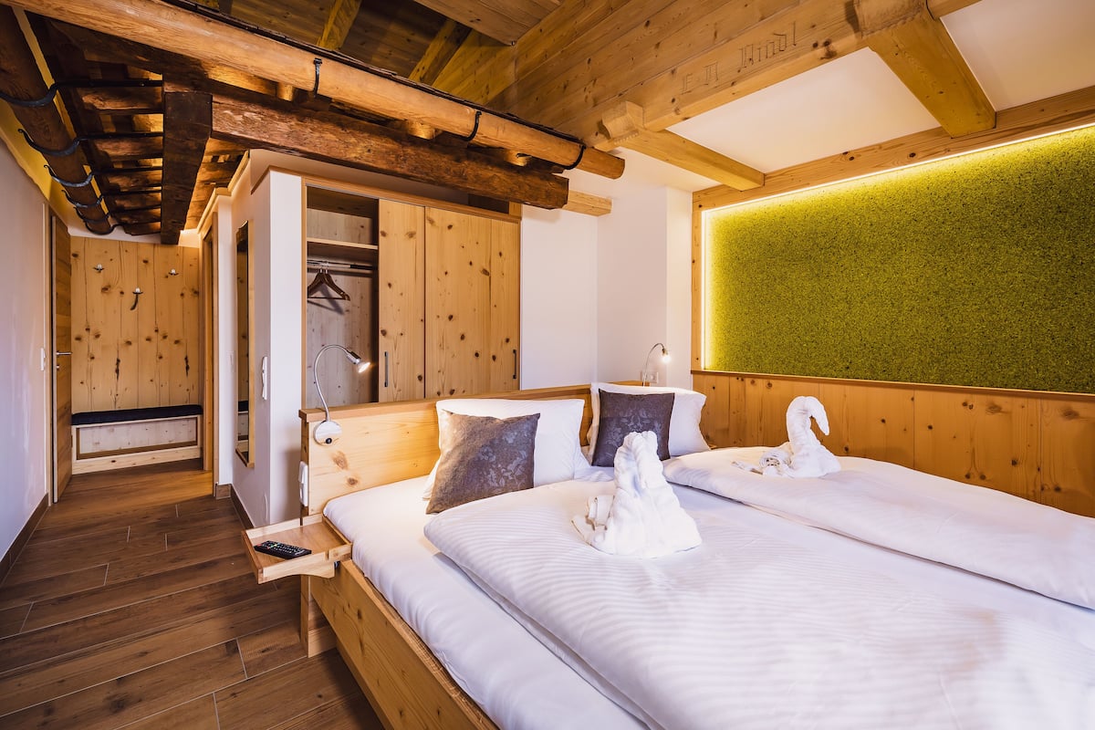 Quarto de madeira com duas camas, um banco e uma parede verde.